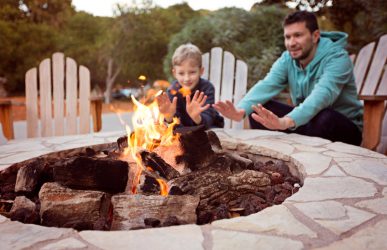 view of firepit and happy smiling family of two, father and son, warming their hands by the fire and enjoying time together in the background
